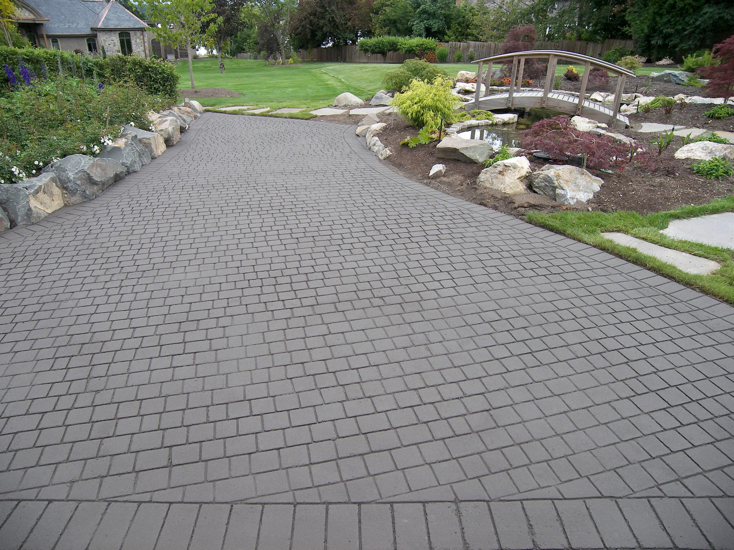 A grey ashlar StreetPrint walkway curving through a garden to the house, installed by Square One