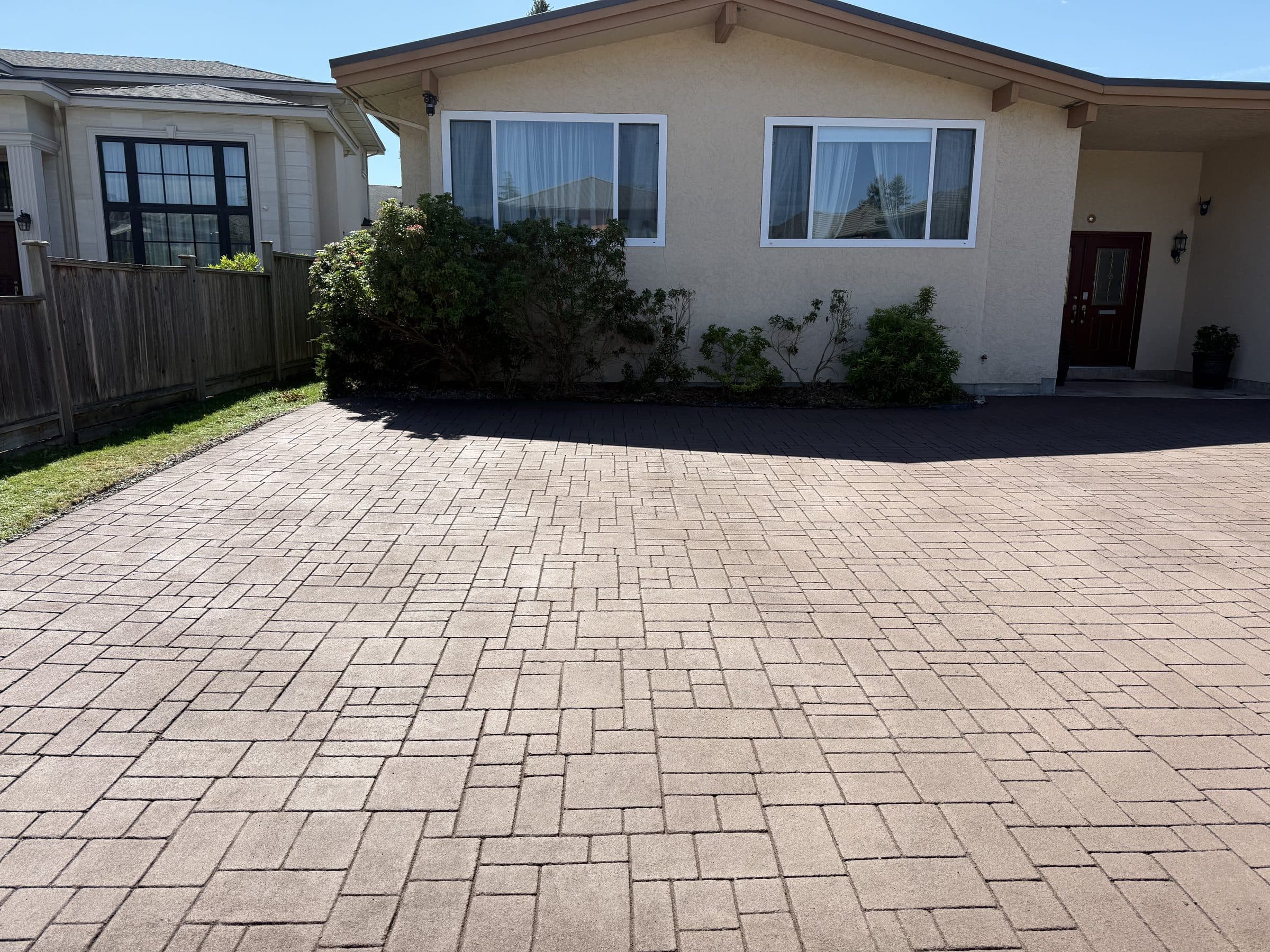 A red-brown brick-pattern StreetPrint driveway in front of a stucco bungalow in Richmond, installed by Square One