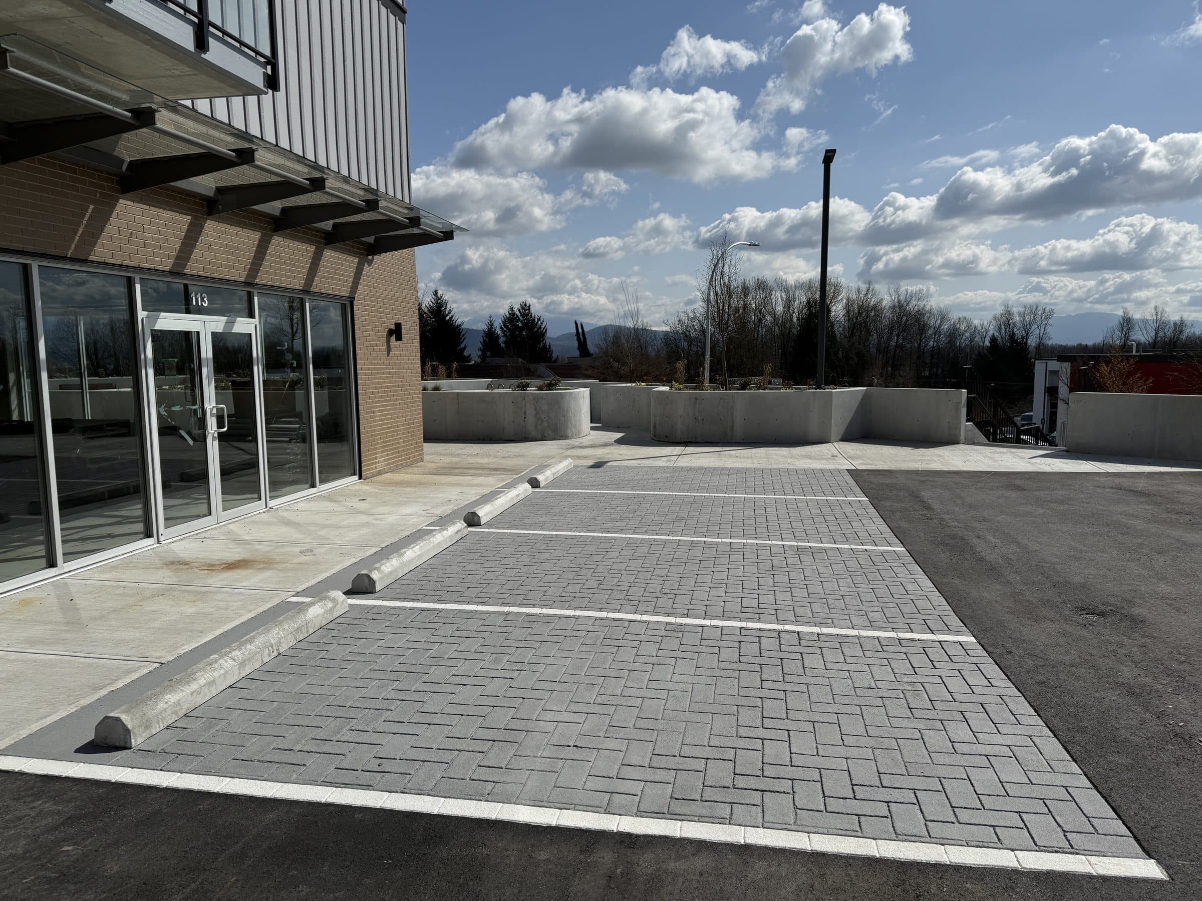 Grey herringbone StreetPrint parking bays in front of a new commercial building in Mission, clouds over the hills beyond